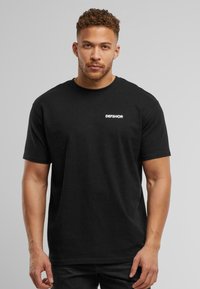 Sort bomulds T-shirt med korte ærmer, rund hals, med et lille hvidt logo "DEFSHOP" på venstre brystområde. Simpelt design.
