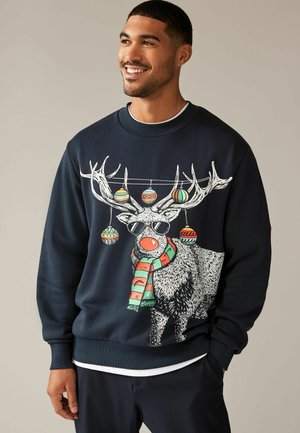 Felpa blu navy con grafica di un renna, le cui corna sono decorate con ornamenti colorati. Include una sciarpa e occhiali da sole. Maniche e orlo a costine.