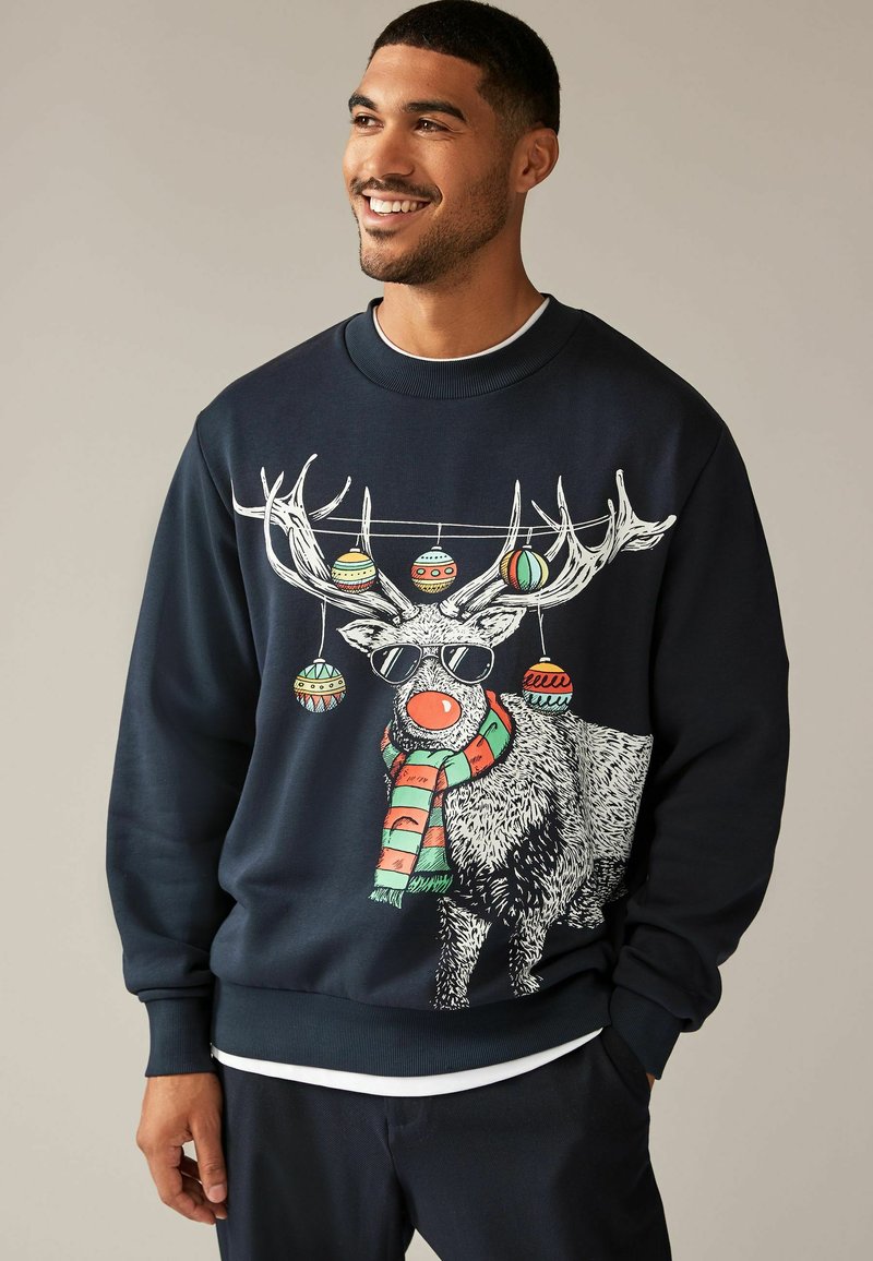 Felpa blu navy con grafica di un renna, le cui corna sono decorate con ornamenti colorati. Include una sciarpa e occhiali da sole. Maniche e orlo a costine.