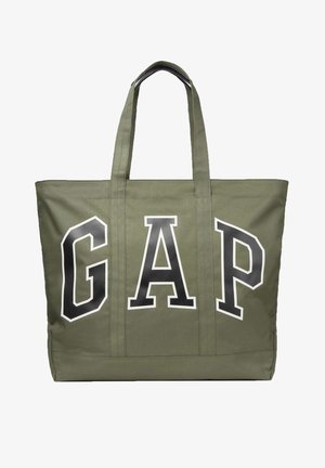 Olijfgroene canvas tote tas met twee handvatten en grote zwarte letters "GAP" met witte omlijning aan de voorkant.