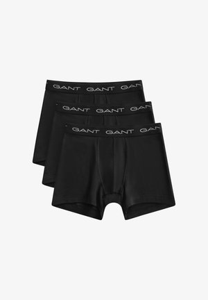 Trois boxers pour hommes noirs empilés, chacun avec une ceinture noire arborant le logo blanc "GANT" répété tout autour.