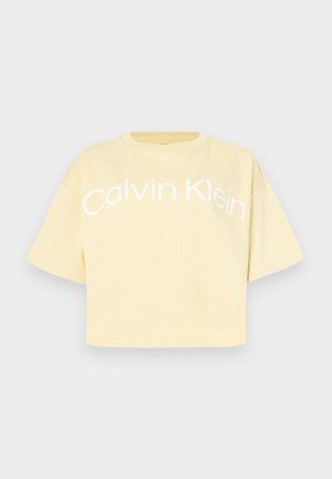 Gul kortermet t-skjorte med "Calvin Klein" trykt med store hvite bokstaver over fronten. Glatt bomullstekstur.