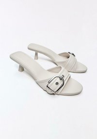 Sandales à talons beige à bout ouvert avec une large bride munie d'une grande boucle argentée et un petit talon kitten.