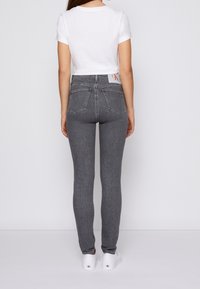 Vaqueros grises de talle alto con un diseño ajustado, que incluyen bolsillos traseros y una etiqueta con marca. Combinados con una camiseta blanca de manga corta y zapatos blancos.