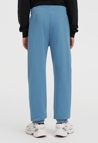 Hellblaue Sweatpants mit lässiger Passform, elastischem Bund und umgeschlagenen Knöcheln. Getragen mit weißen und grauen Sportschuhen.