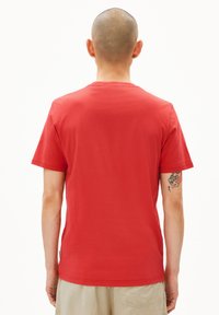 Rode katoenen t-shirt met korte mouwen, ronde hals en een eenvoudige achterkant. Opvallende armtatoeages zichtbaar, met een losse pasvorm.