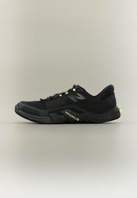 Μαύρο αθλητικό παπούτσι New Balance Minimus με επάνω μέρος από δίχτυ, αντανακλαστικό λογότυπο και πράσινες φωσφορίζουσες λεπτομέρειες στη σόλα και στα κορδόνια.