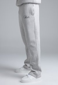 Grijze joggingbroek van zacht materiaal, met een slim fit, zijzakken en een klein logo in marineblauw op de linker heup. Gecombineerd met witte sneakers.