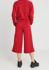 Röd idrottsoutfit bestående av en tröja med rund halsringning och korta byxor. Tyget är slätt med en ribbad fåll. Svarta sneakers fulländar looken.