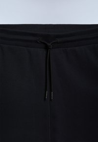 Mustat collegehousut, joissa on joustava vyötärönauha ja kiristysnauha. Sileä pinta ja tiukat resorit lahkeensuissa. Kiristysnauhojen päissä on logo.