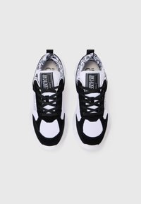 Svart og hvit sneaker med en blanding av glatte og teksturerte materialer, tykk hvit såle og intrikat mønstret krage med snøring.