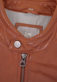 Braune Lederjacke mit hohem Kragen, silbernem Druckknopf und Reißverschluss; glatte Textur mit sichtbaren Nähtendetails.