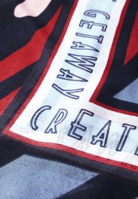 Gemusterter Stoff in kräftigen Rot-, Schwarz- und Blautönen, mit den Worten "Verschwinde" und "Kreativ" in kontrastierenden Schriftstilen.