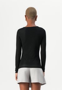 Top negro de manga larga con un patrón texturizado, diseño ajustado, escote redondo, combinado con una falda clara de corte acampanado en gris claro.