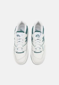 Paire de baskets New Balance 550 blanches et vertes avec lacets, vues de dessus sur un fond clair uni.