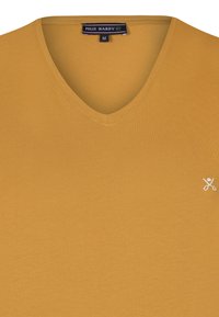 Žluté tričko s výstřihem do V vyrobené z měkké tkaniny, s malým bílým logem nůžek na levé straně, velikost M. Hladká textura a minimalistický design.