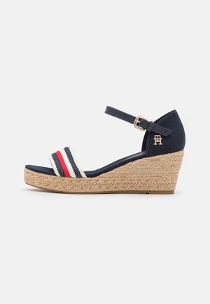 Sandale compensée marine avec boucle à la cheville, plateforme en jute tressé et bride avant à rayures rouge, blanc et bleu.