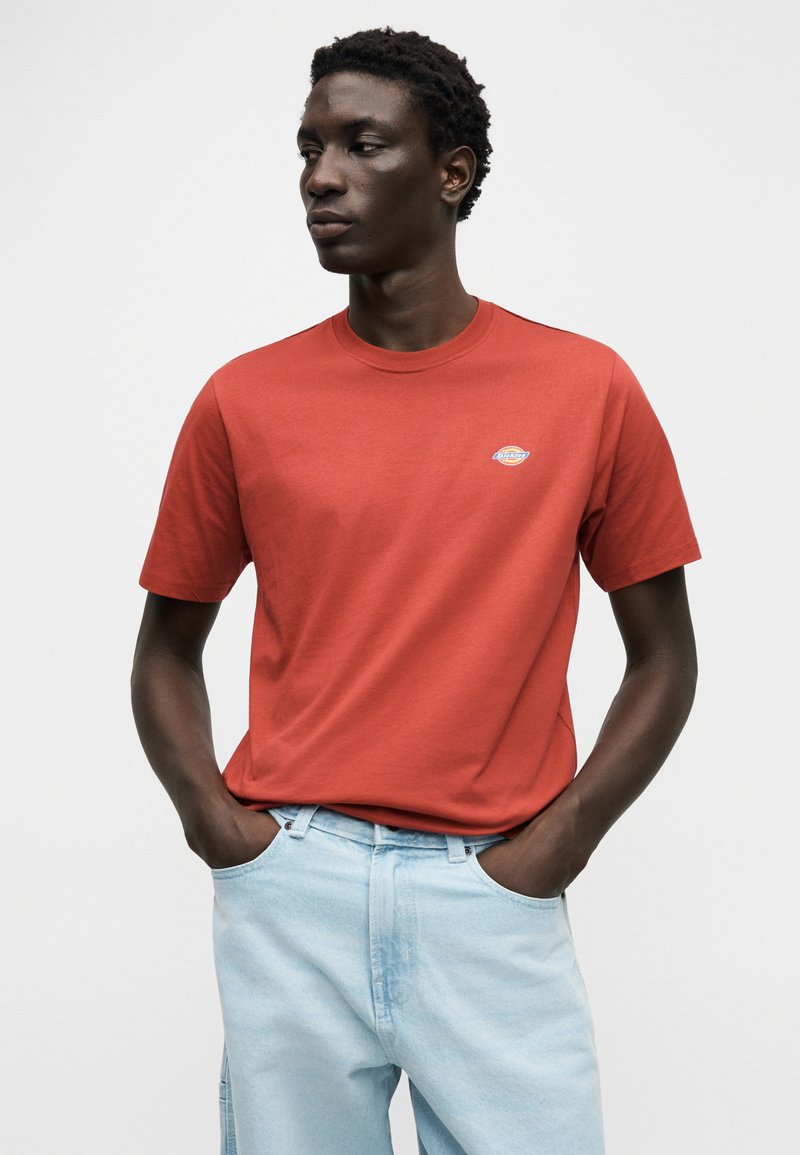 Rood katoenen T-shirt met een ronde hals en korte mouwen, voorzien van een klein geborduurd logo op de borst, gecombineerd met lichtblauwe jeans.