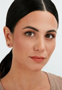 Runde Steckerohrringe mit einem dunkelblauen Edelstein, getragen von einer Person mit dunklem Haar, die ein natürliches Makeup trägt und ein Top in neutralen Farbtönen.