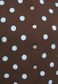 Material maro cu buline albastre deschise distribuite uniform și un rând vertical de nasturi mici, rotunzi, translucizi.