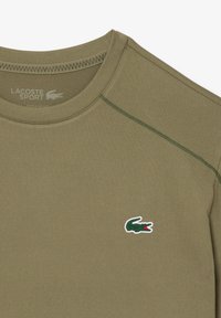 Tricou sportiv de culoare verde măslină, fabricat dintr-un material moale, având un guler rotund și accente verzi cusute, cu un mic logo brodat de crocodil.