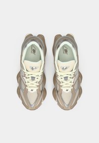 Bež i sivi tenisice imaju mrežasti i zamršeni materijali, s debelim potplatom, okruglim vrhom i kremastim vezicama. Značajno brendiranje na jeziku.