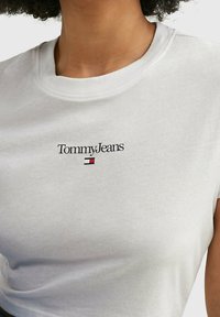 Bílá bavlněná tričko s černým logem "Tommy Jeans" a červenou a modrou akcentovou krabicí pod ním. Krátké rukávy a kulatý výstřih.