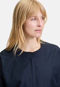 Veste légère bleu marine avec un col rond et des coutures minimales. Texture lisse, équipée d'une fermeture éclair et sans motifs visibles.
