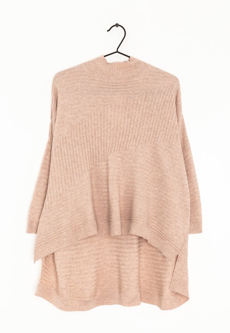 Lichtbeige oversized sweater met geribbelde textuur, hoge hals en asymmetrische zoom. Het materiaal lijkt zacht en comfortabel. Hangt aan een zwarte haak.