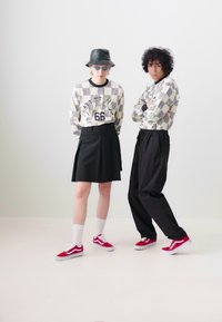 To modeller har mønstrede langermede skjorter, et svart skjørt og løse svarte bukser, kombinert med røde sneakers og hvite sokker.