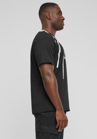 Sort T-shirt med korte ærmer, der har et hvidt lynlåsdesign foran. Materialet ser glat ud, og pasformen er afslappet.