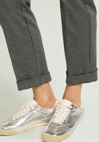 Zapatillas metálicas plateadas con cordones color crema y suela texturizada, combinadas con pantalones dobles de tono gris oscuro. Enfoque en líneas limpias y diseño minimalista.