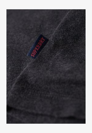 T-shirt in cotone grigio scuro con una piccola etichetta blu con "SUPERDRY" in rosso. Texture liscia con un delicato motivo a trama.