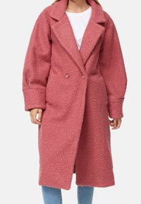 Manteau rose texturé à double boutonnage, grand col à revers et manches longues, descendant sous le genou. Tissu doux et confortable.