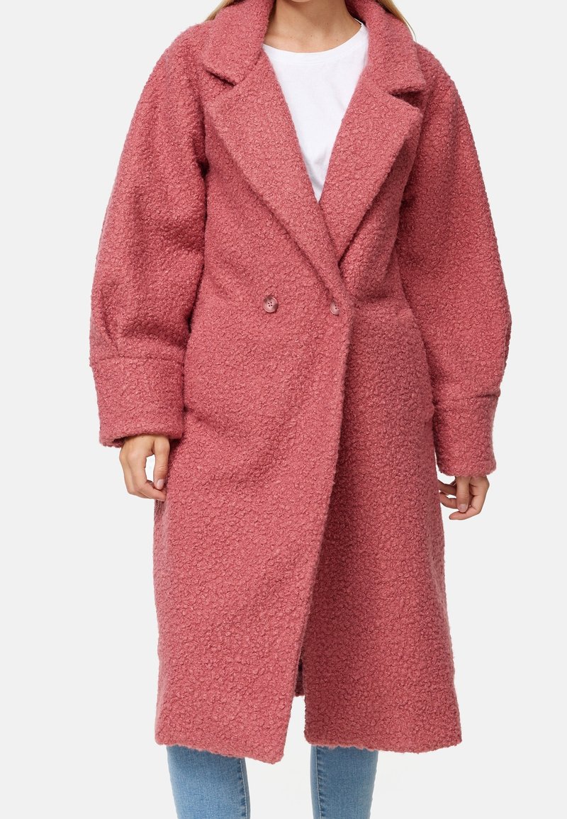 Manteau rose texturé à double boutonnage, grand col à revers et manches longues, descendant sous le genou. Tissu doux et confortable.
