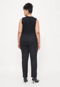 Black sleeveless top paired with black tailored pants. Smooth fabric, fitted silhouette, with ankle-length pants and high-heeled shoes.