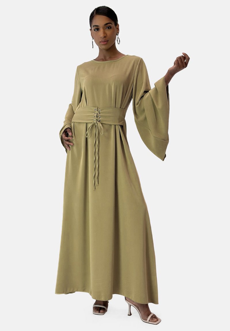 Abito lungo in verde oliva, realizzato in tessuto morbido. Presenta maniche a campana lunghe, vita cintrata con dettaglio delle stringhe e una silhouette fluida.