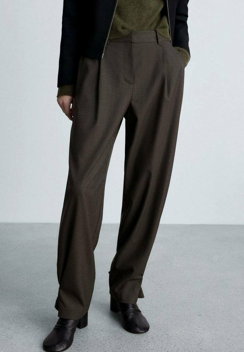 Pantaloni larghi marroni con vita alta, design minimalista e texture liscia. Abbinati a una giacca scura e a un top aderente.
