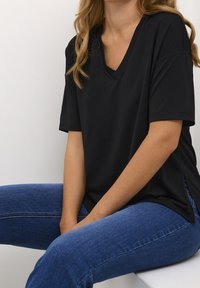 T-shirt nera a maniche corte a V in morbido tessuto, con spacchi laterali per facilitare i movimenti, abbinata a jeans in denim blu.