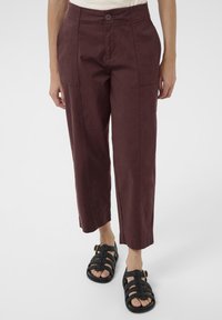 Bordeaux gekorte broek met een relaxed fit, voorzien van zijzakken en een knoopsluiting; gecombineerd met zwarte sandalen met bandjes.