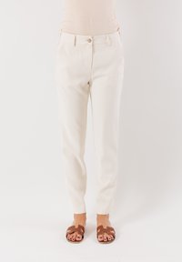 Pantaloni color crema con vestibilità dritta, dotati di tasche frontali, chiusura a bottone e superficie liscia. Abbinati a sandali a scivolo marroni.