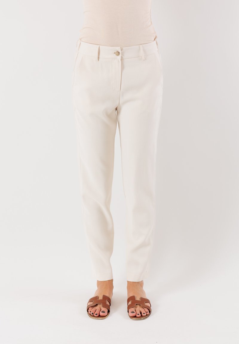 Pantaloni color crema con vestibilità dritta, dotati di tasche frontali, chiusura a bottone e superficie liscia. Abbinati a sandali a scivolo marroni.