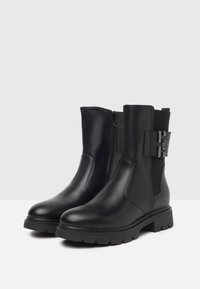 Black leather ankle boots with a side zipper, elastic panel, chunky sole, and a decorative accent on the outer side. Flat heel design.
