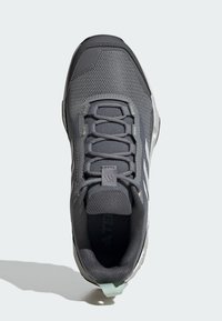 Pantofii sport gri prezintă un superior din plasă, material texturat, vârf rotunjit și accente subtile de branding. Include un toc curbat și închidere cu șiret.