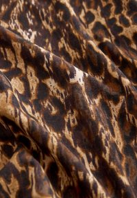 Tissu imprimé léopard marron et noir avec des plis doux et une apparence texturée et veloutée.