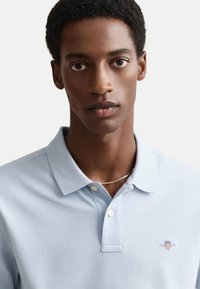 Lichtblauw poloshirt van een katoenmix, met een klassieke kraag, een knoopsluiting met twee knopen en een klein geborduurd logo op de borst.