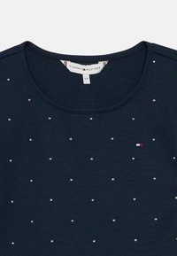 Sötétkék Tommy Hilfiger ing apró ezüst szegecsekkel, amelyek a szöveten szétszórva találhatók, és egy kis piros, fehér és kék logóval a mellrészén.