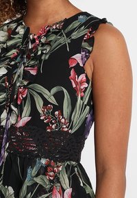 Robe sans manches à fleurs avec un fond noir, arborant des motifs botaniques colorés et une bande en dentelle texturée à la taille.