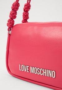 Rosa Handtasche aus Kunstleder mit geflochtenem Griff, ausgestattet mit dem silbernen "LOVE MOSCHINO"-Logo. Glatte Textur und minimalistisches Design.