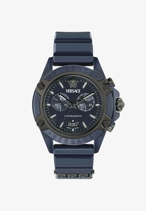 Versace kronografska ura z mornarsko modrim silikonskim trakom, velikim okroglem ohišjem, mat črnimi poudarki, dvojimi sub-števci in reliefnim logotipom na obroču.